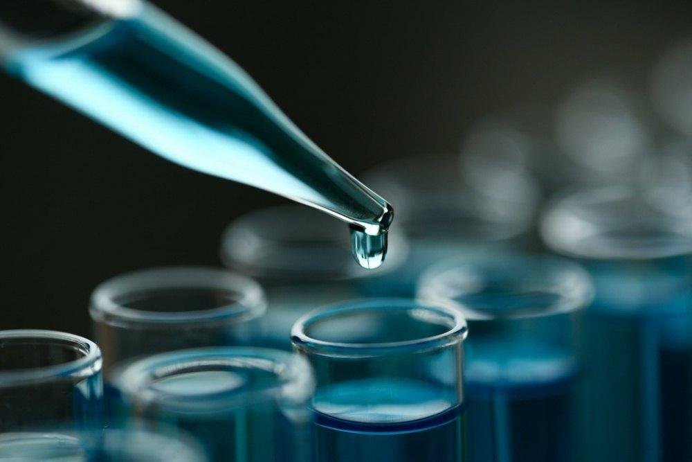Laboratory pipette dropping blue chemical solution into test tubes